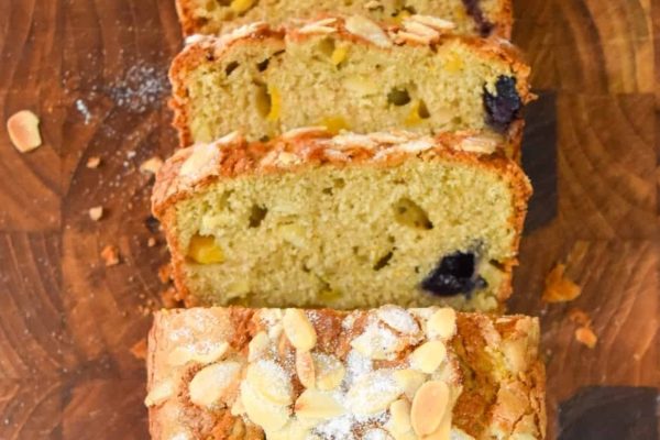 A loaf of bread with blueberries and almonds on a cutting board.