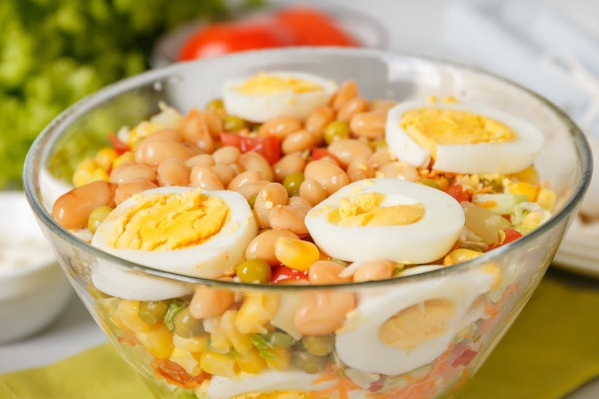 A bowl of salad with eggs, beans and corn.
