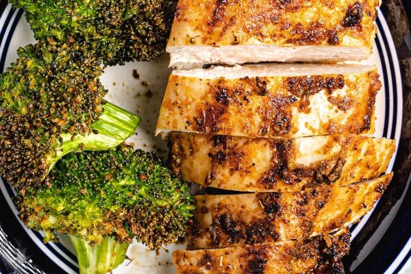 A piece of chicken on a plate with broccoli.