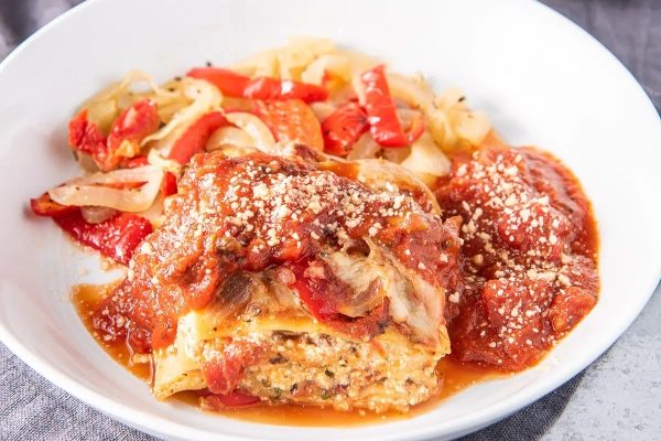 A white bowl filled with lasagna and vegetables.