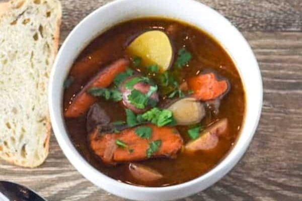 A bowl of stew with potatoes, carrots and bread.