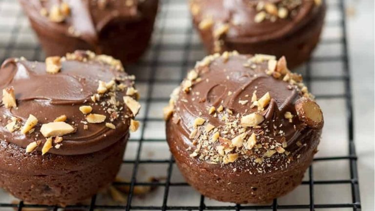 Four chocolate muffins with nuts on a cooling rack.