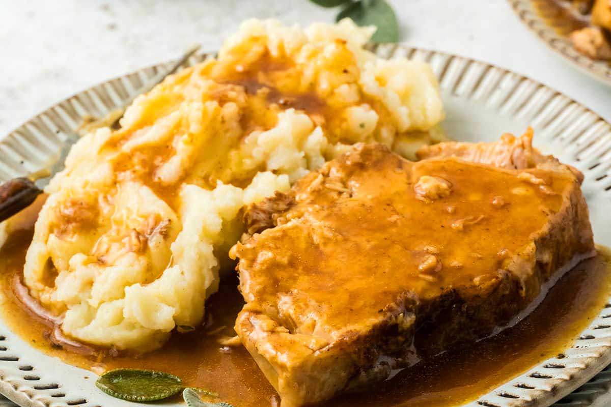 Pork tenderloin with gravy and mashed potatoes on a plate.