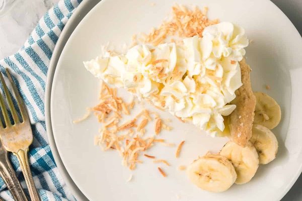A slice of coconut pie with whipped cream and bananas on a plate.