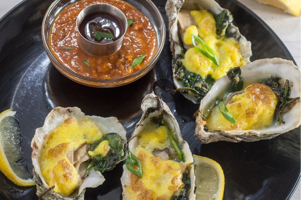 Seven Fishes feast featuring stuffed oysters with chorizo and spinach on a black plate.