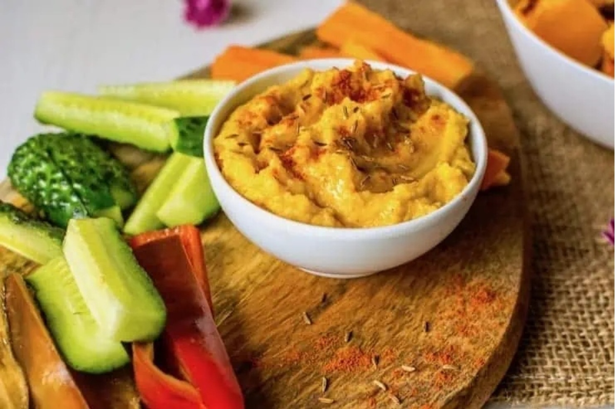 An appetizing bowl of hummus and vegetables on a wooden cutting board, perfect for New Year's Eve festivities.