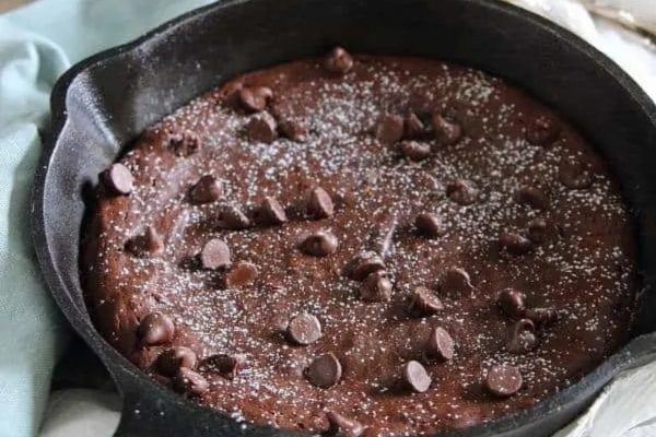 A brownie cake in a cast iron skillet with powdered sugar.