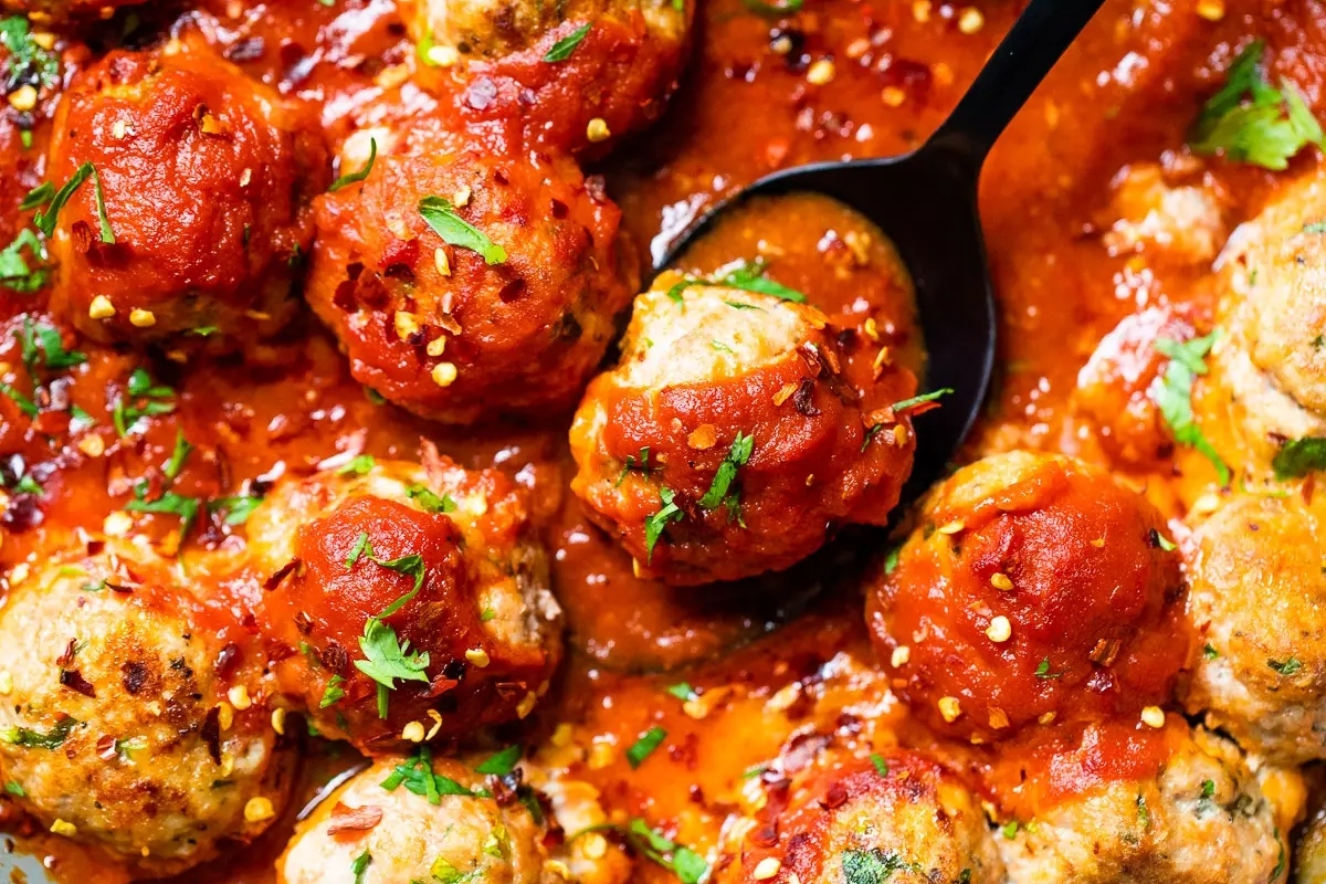 Ground turkey meatballs in tomato sauce, served with a spoon.
