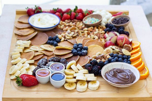 A wooden board with fruit, nuts, and dips on it.