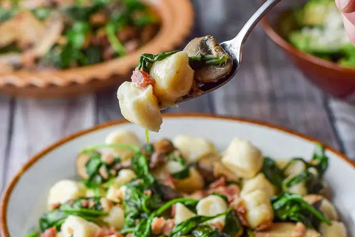 A spoon full of gnocchi with spinach and mushrooms.