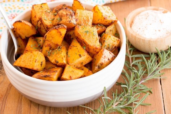 Roasted sweet potatoes in a white bowl with sprigs of rosemary.