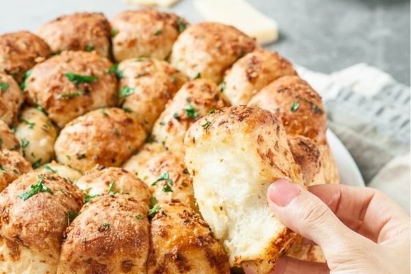 A person taking a bite out of a cheesy bread.