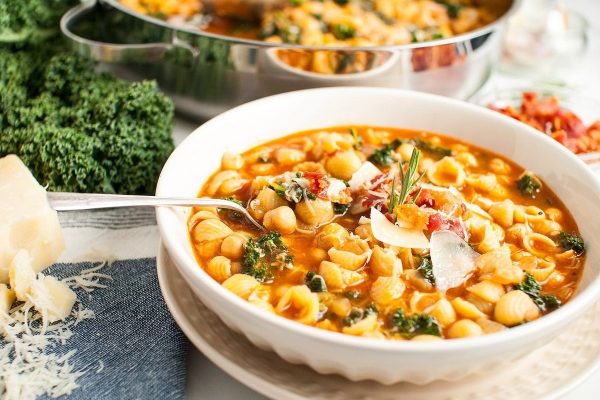 A bowl of pasta and kale soup, made with a few ingredients, served with a spoon.