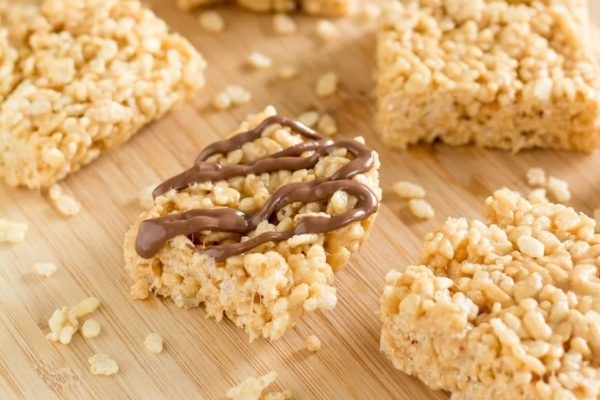Rice krispy treats with chocolate drizzle on a cutting board.