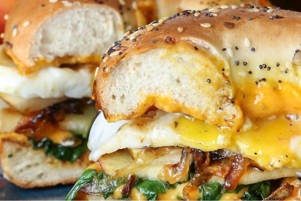 A bagel sandwich with eggs, spinach and cheese.