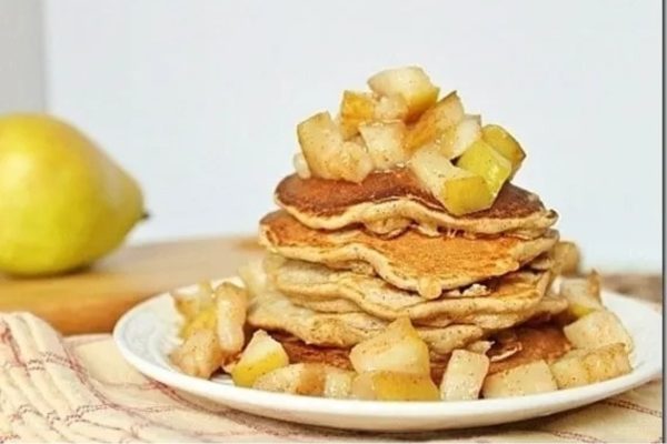 A stack of pancakes with pears and apples on a plate.
