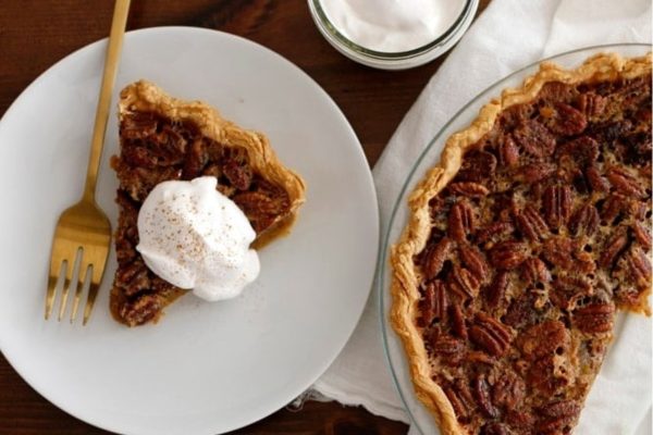 A slice of pecan pie on a plate with whipped cream.