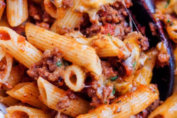 A close up of a bowl of penne pasta with meat and cheese.