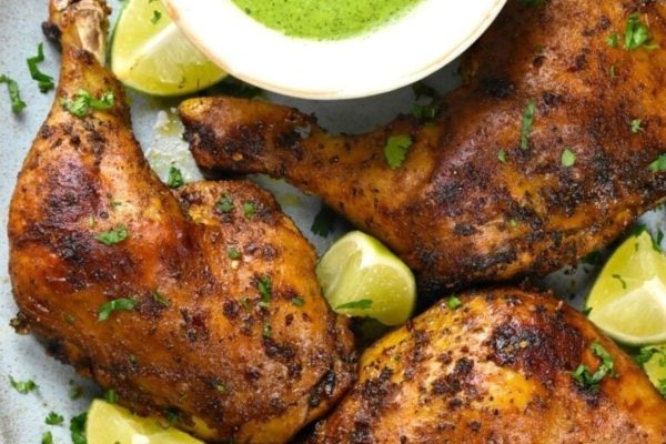 Chicken thighs with lime sauce and lime wedges on a plate.