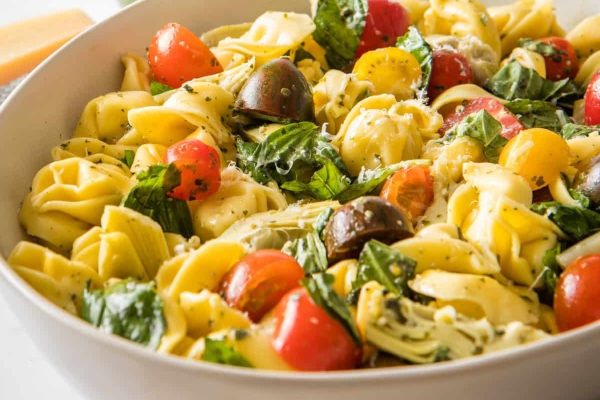 A white bowl of pasta salad with tomatoes and basil.