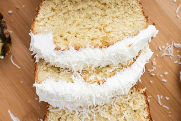A slice of coconut cake on a cutting board.