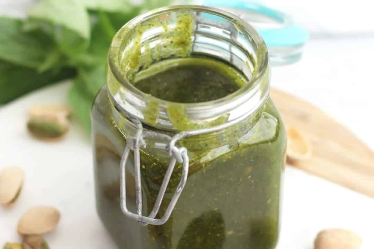 A jar of pistachio pesto on a wooden cutting board.