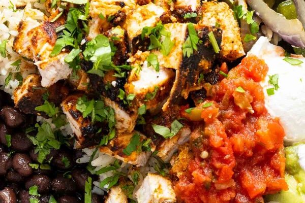 A bowl of mexican food with chicken, rice and black beans.