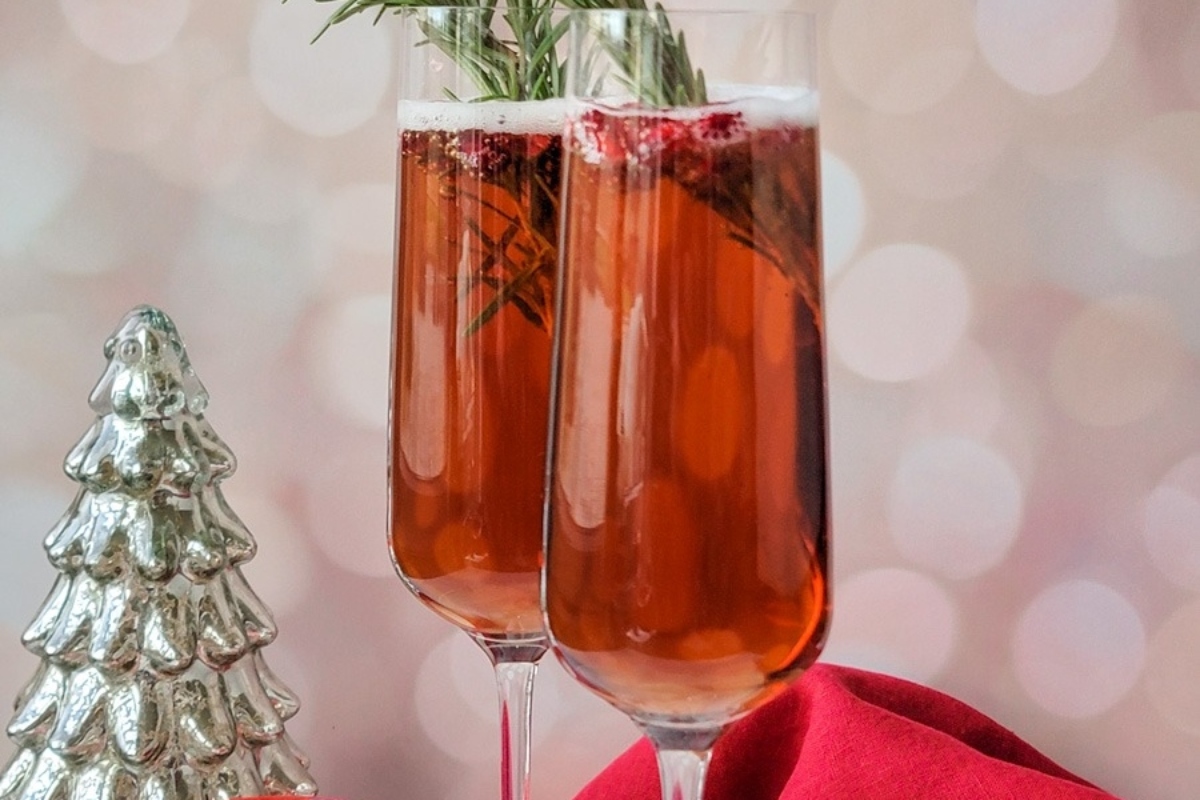 Two champagne cocktails with pomegranate and rosemary garnishes.