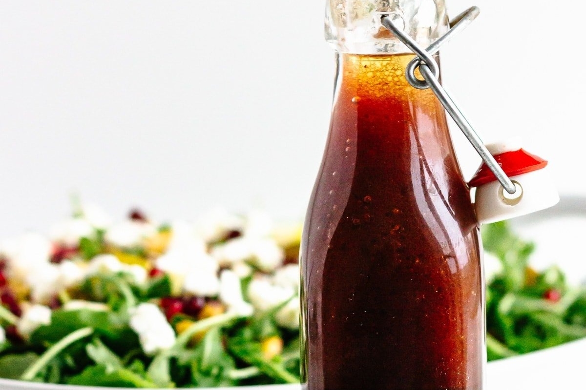 A bottle of pomegranate balsamic vinaigrette next to a salad.