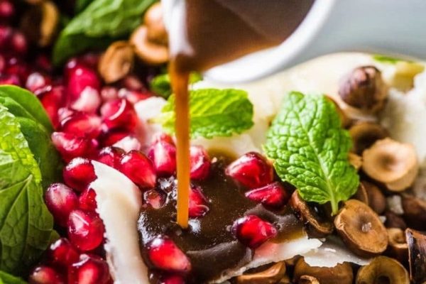 Pomegranate dressing being poured over a salad with nuts and pomegranate.