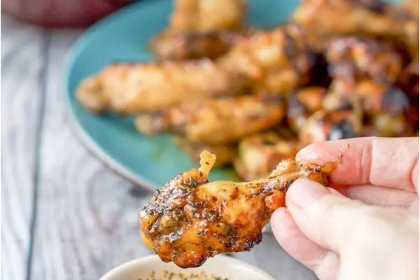 A person is dipping chicken wings into a bowl of sauce.