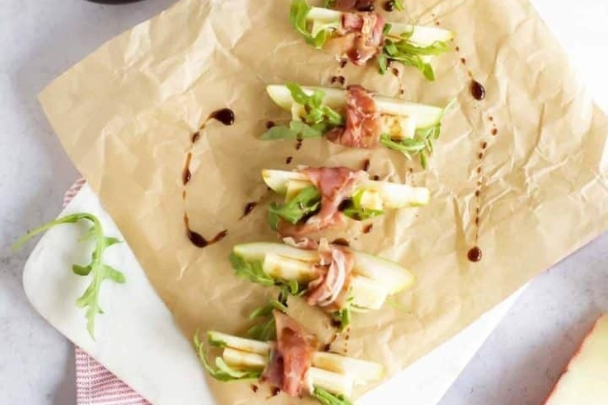 Party appetizers featuring apple and arugula on a brown paper plate.