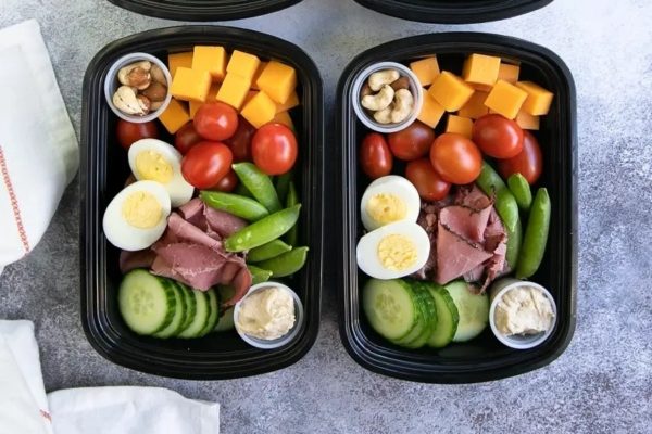 Two black containers with ham, eggs, tomatoes and cheese.