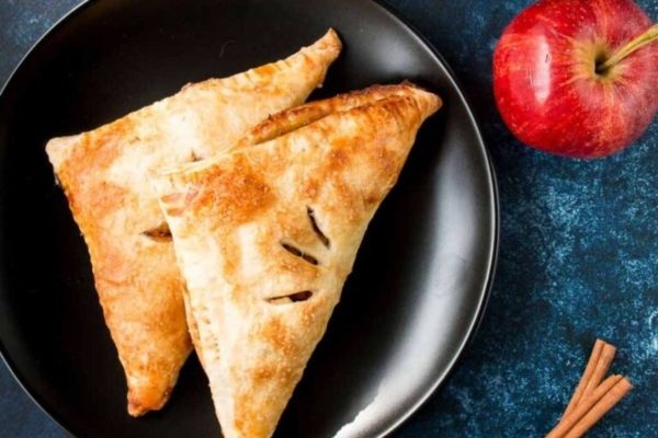 Two apple pies on a plate with cinnamon sticks.