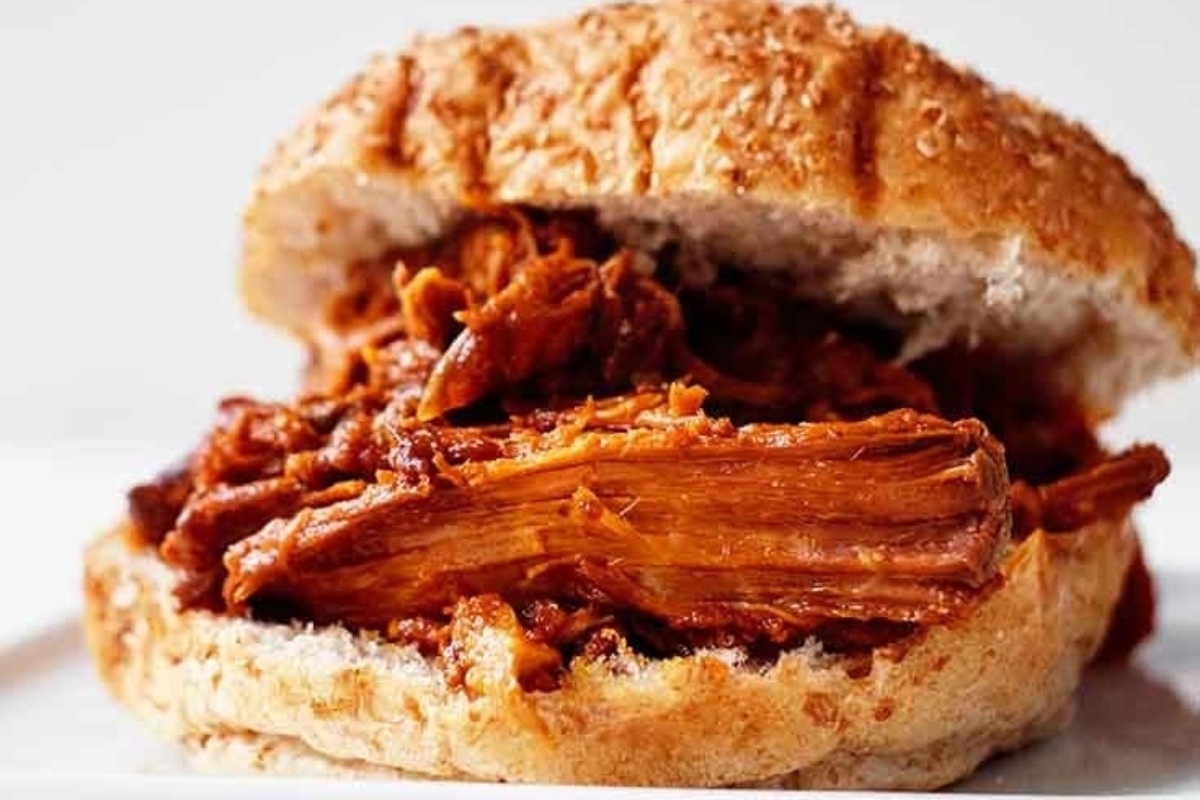 A slow cooker pulled pork sandwich on a white plate.