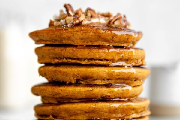 A stack of pumpkin pancakes with syrup and pecans.