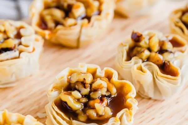 Walnut tartlets with caramel sauce on a wooden cutting board.