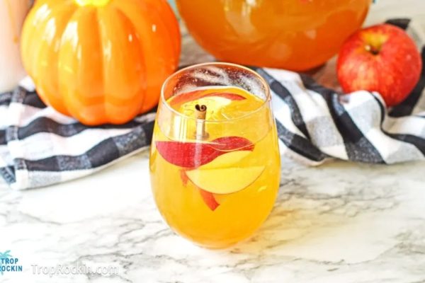 A glass of apple cider punch with apples and pumpkins.