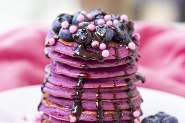 A stack of pancakes with blueberries and chocolate drizzle.