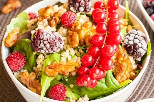 A colorful bowl of quinoa salad with berries and walnuts.