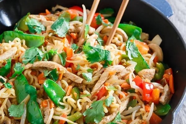 Stir fried ramen noodles with chicken and vegetables in a skillet.