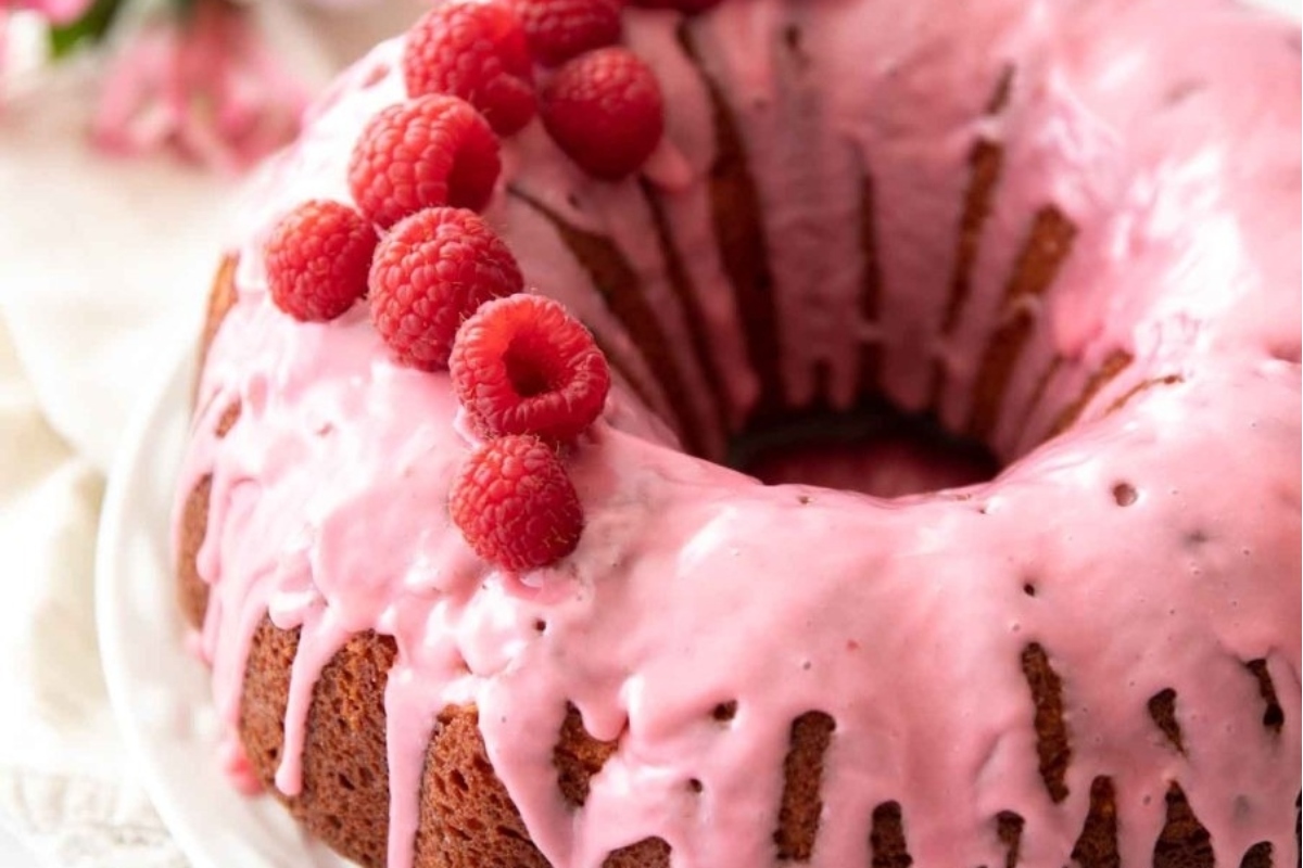 A pink bundt cake with icing and raspberries, perfect for special occasions. It is a delightful twist on traditional bundt cakes, showcasing a vibrant hue and topped with a luscious