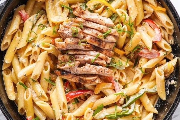 Grilled chicken pasta in a skillet with peppers and herbs.