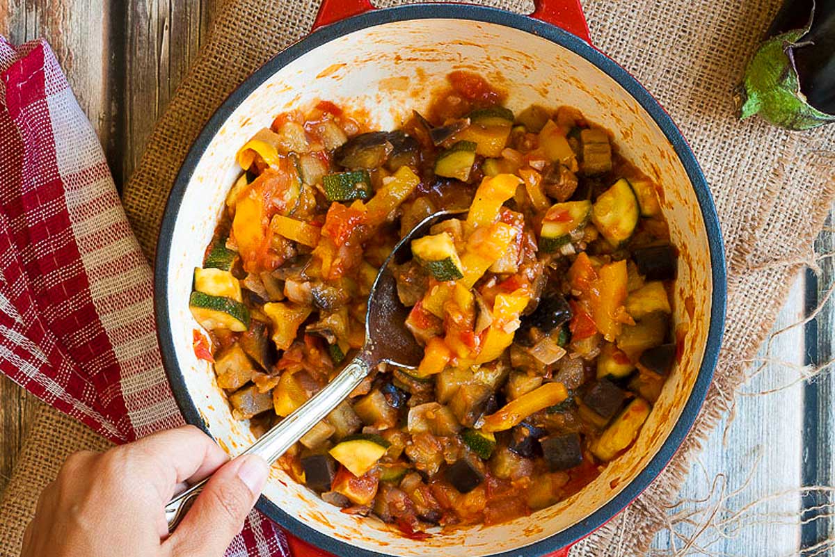 A person is taking a spoonful of tomato vegetables out of a pan.