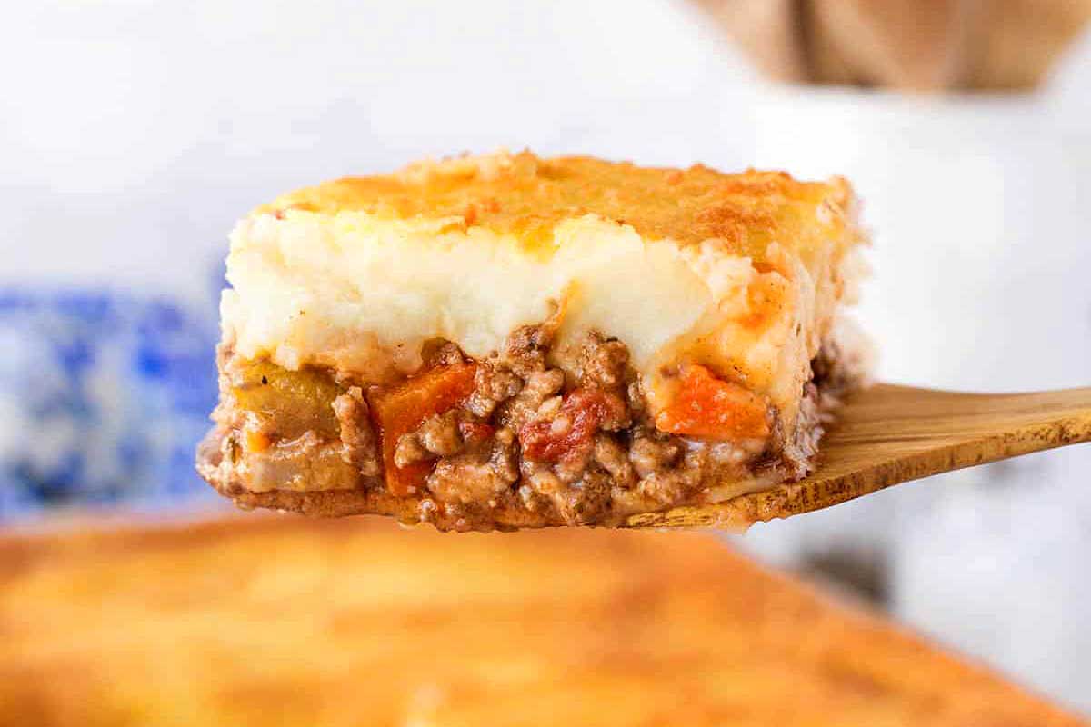 A wooden spoon is holding a piece of shepherd's pie.