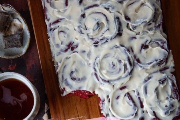 A slice of decadent red velvet cake on a wooden cutting board.