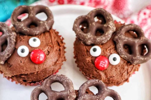 Christmas cupcakes adorned with chocolate reindeer and pretzels on a festive plate.