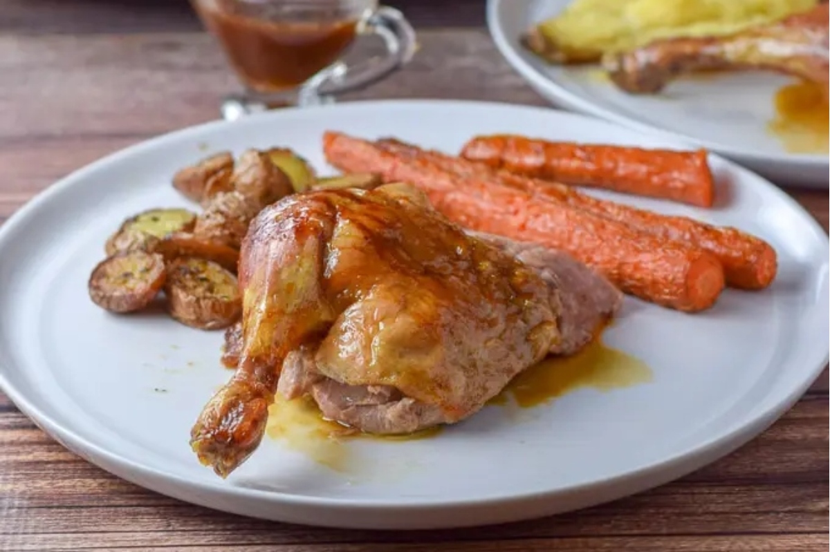 Roasted duck with carrots and gravy on a white plate.