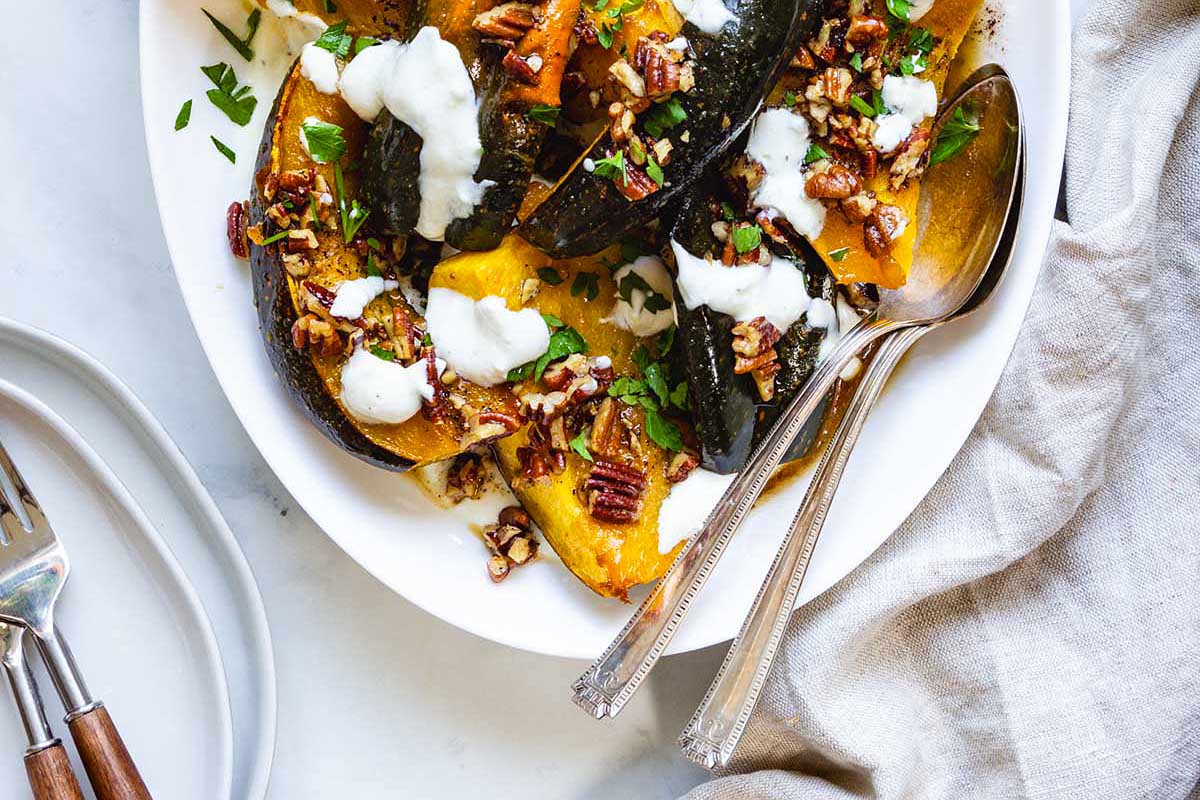 Roasted acorn squash with sour cream and pecans on a white plate for a friends giving feast.