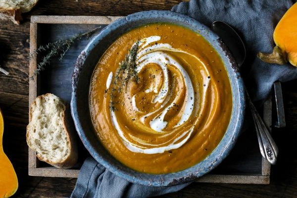 A cheap potluck dish for Thanksgiving, this pumpkin soup is served with a dollop of sour cream and bread.